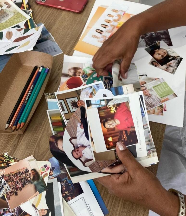 Sessão de arteterapia em andamento: mãos separando recortes de revista para uma colagem, ao lado de uma caixa de lápis de cor